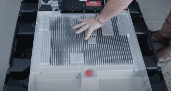 A hand resting on the vented top of a large battery pack, with electronic components visible in the background.